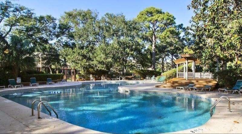 Apartment or condo units with light brown siding and balconies, viewed across a grassy area and trees.