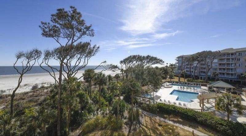 An aerial view of the Hampton Place complex, showing multiple buildings, a large swimming pool, and landscaped grounds near the ocean.