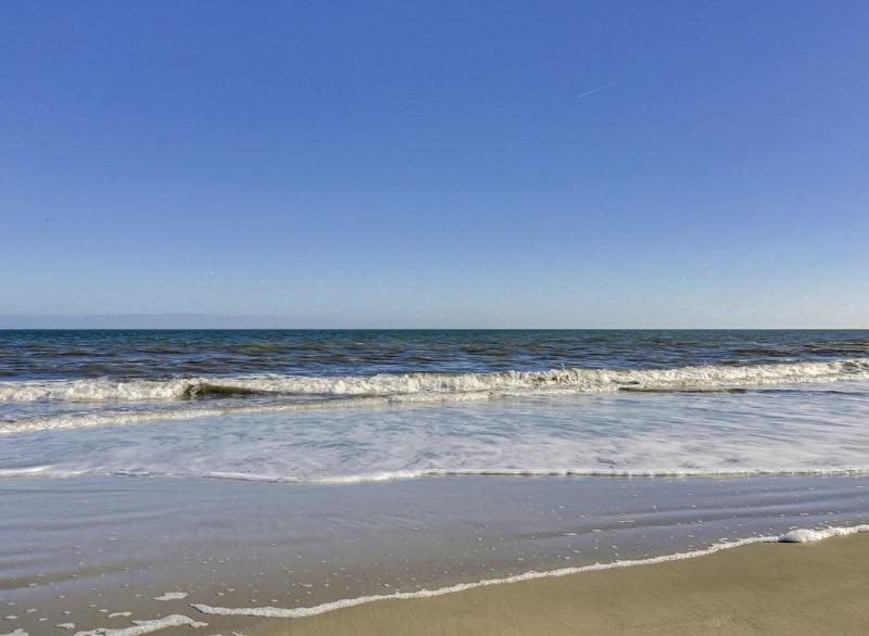 A beach with ocean waves rolling onto the sand under a clear blue sky.