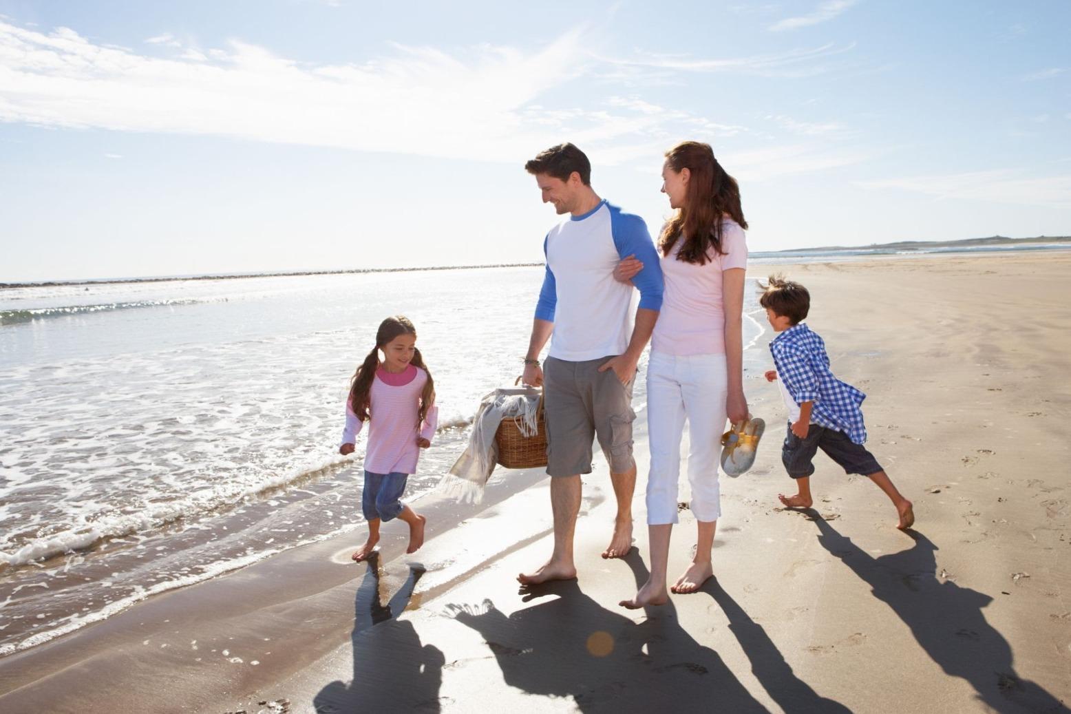 A family of four walking on the beach with a picnic basket