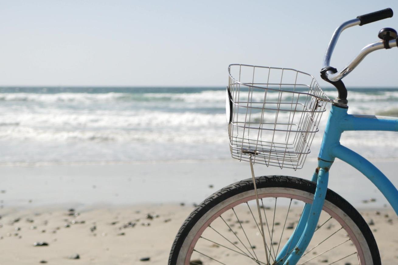 Blue beach cruiser bicycle with a basket parked in the sand.
